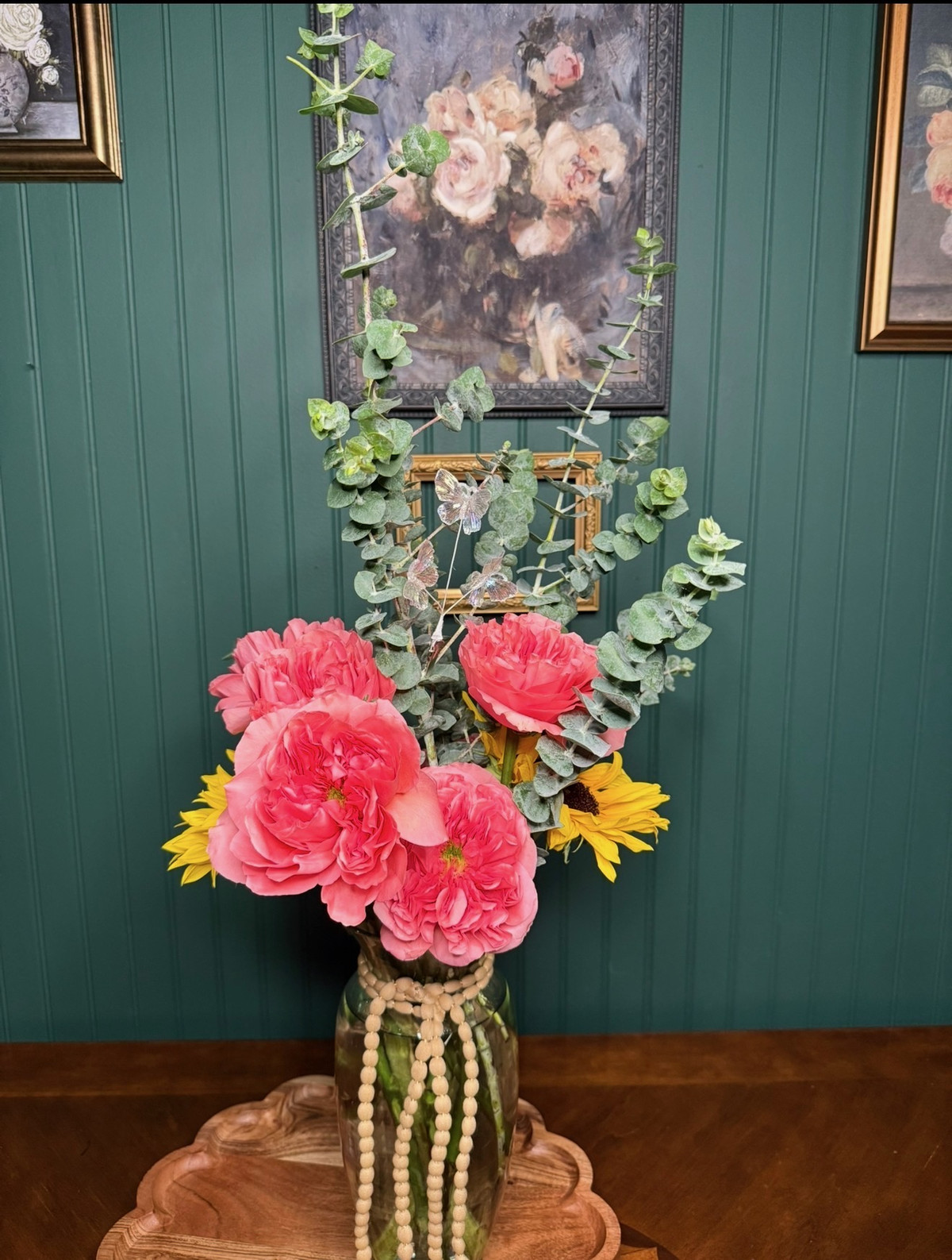 Coral garden roses and sunflowers with eucalyptus in a beaded glass vase