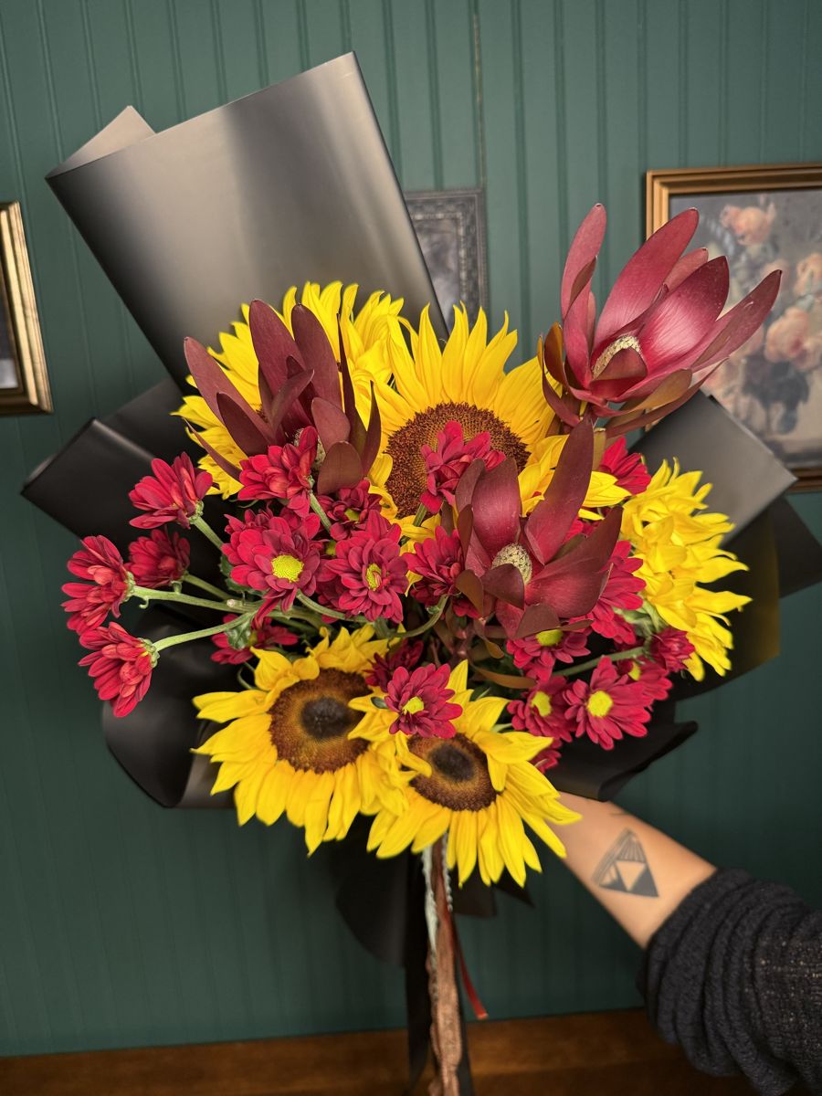 Sunflowers, red mums and leucadendron wrapped in black paper