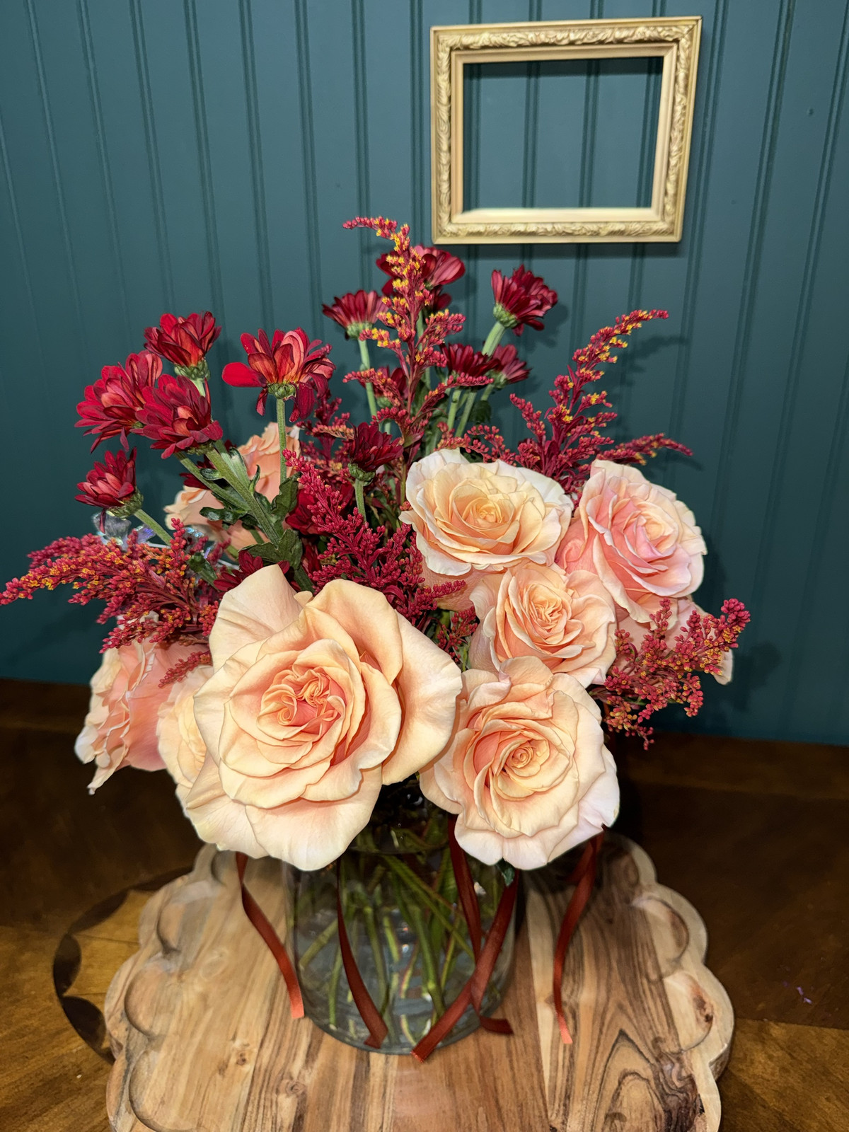 Peach roses with red mums and red solidago in a glass vase