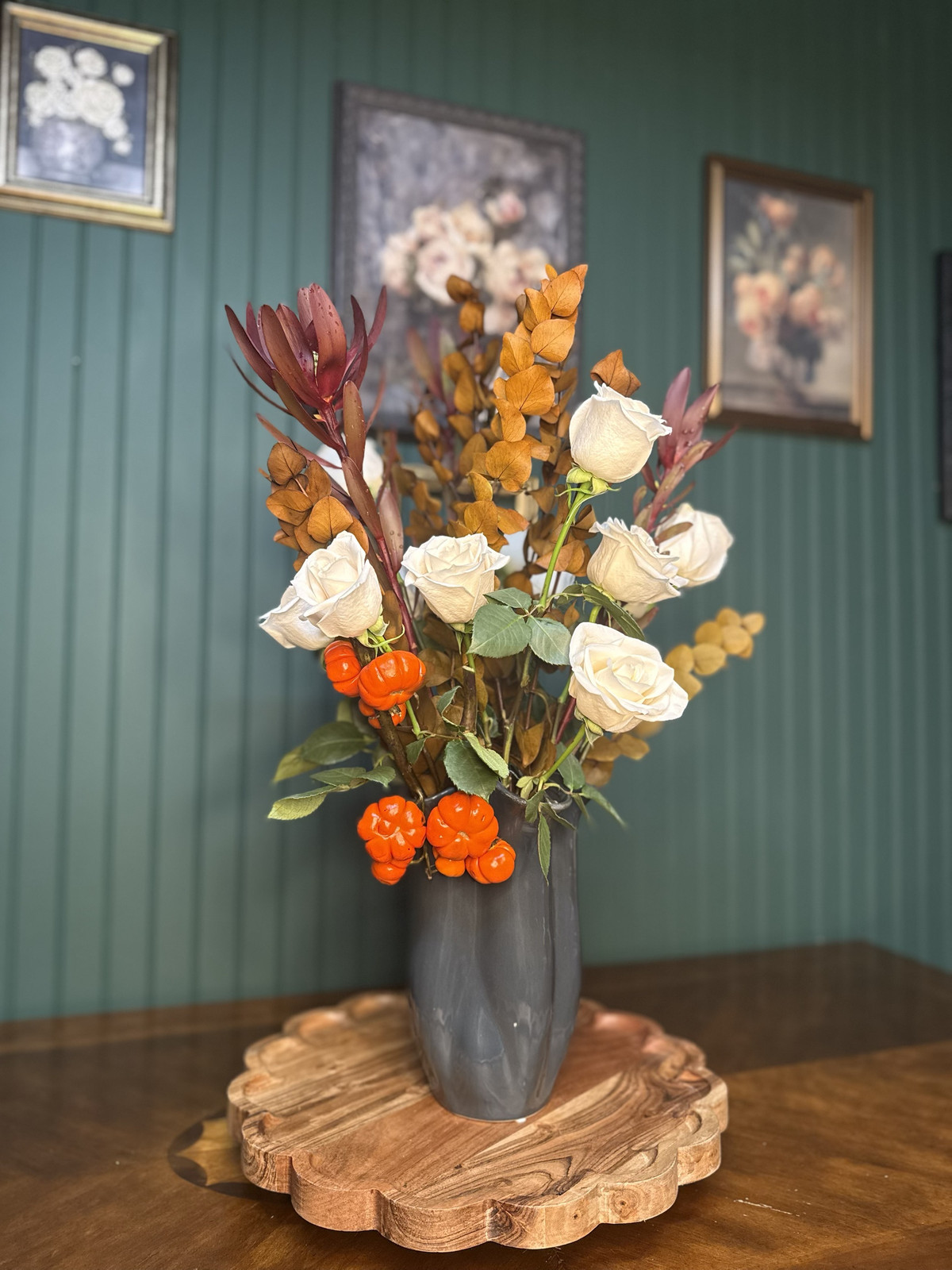 White roses with autumn eucalyptus, burgundy leucadendron and mini pumpkins in a gray vase